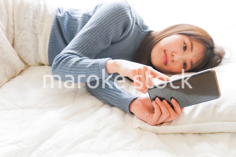 ベッドで寝る前にスマホを使う若い女性