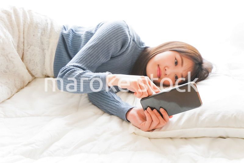 ベッドで寝る前にスマホを使う若い女性