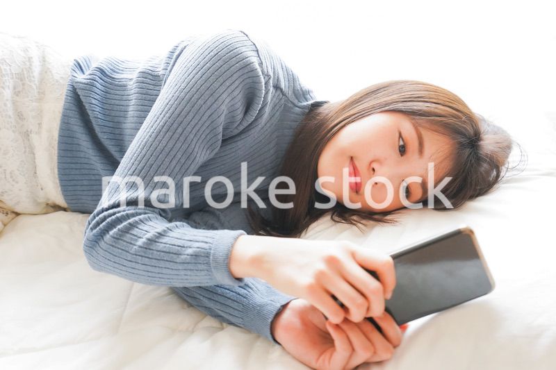 ベッドで寝る前にスマホを使う若い女性
