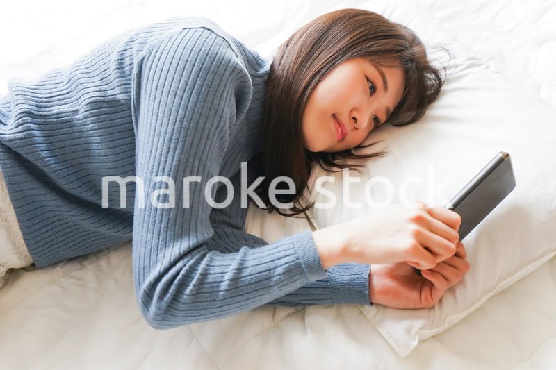 ベッドで寝る前にスマホを使う若い女性
