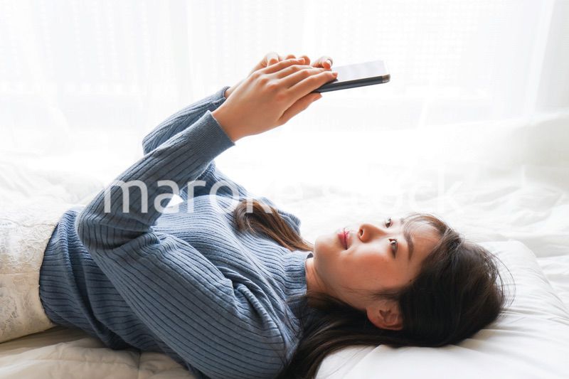 ベッドで寝る前にスマホを使う若い女性