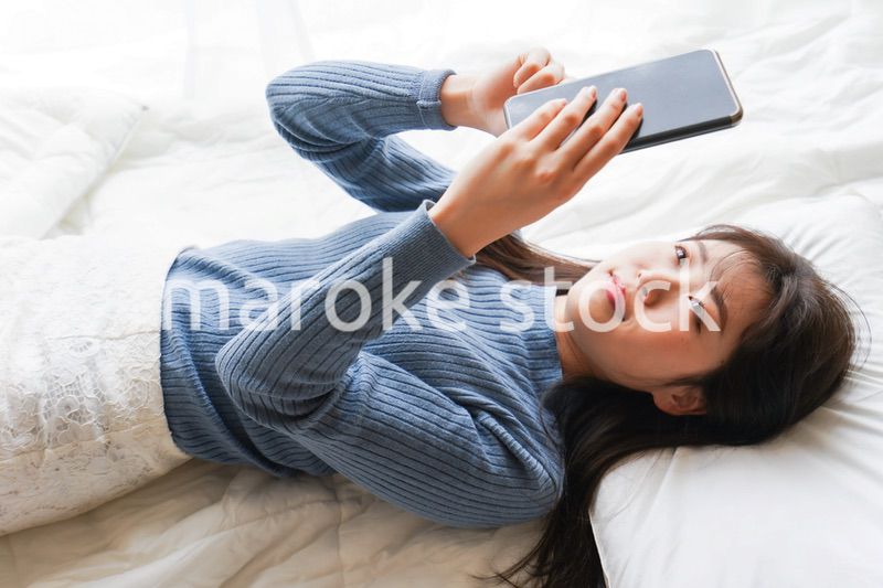 ベッドで寝る前にスマホを使う若い女性
