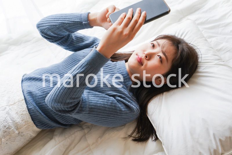 ベッドで寝る前にスマホを使う若い女性