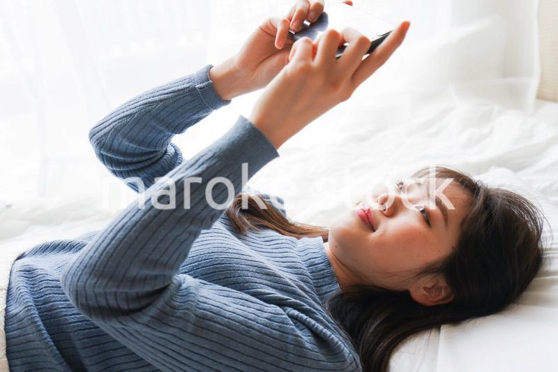 ベッドで寝る前にスマホを使う若い女性