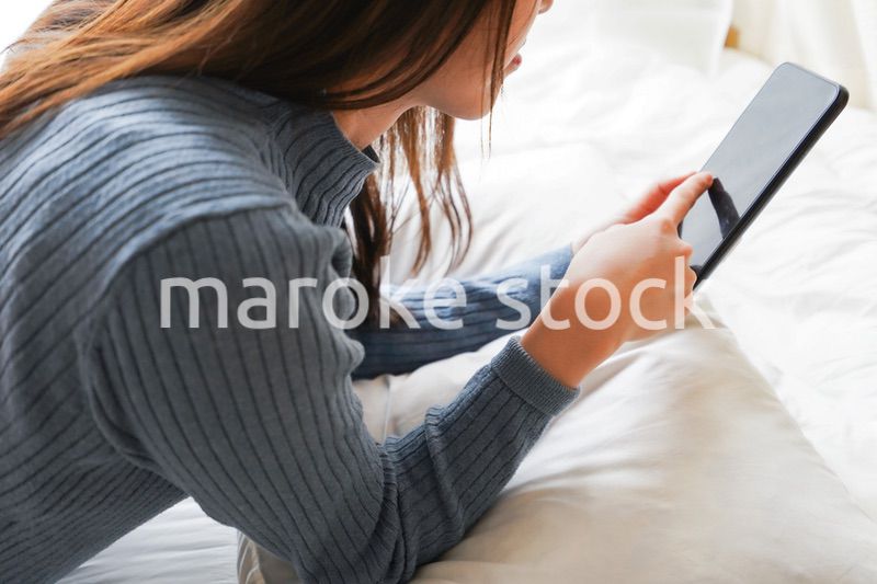 ベッドで寝る前にスマホを使う若い女性