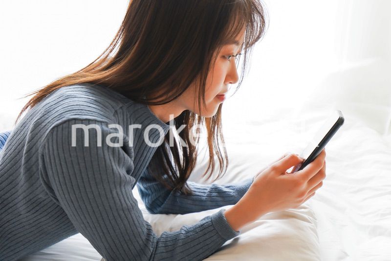 ベッドで寝る前にスマホを使う若い女性