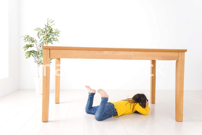 机の下に避難する子ども
