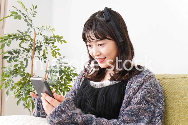 家でスマートフォンを使う若い女性