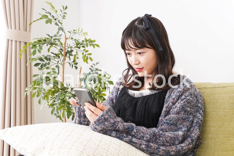 家でスマートフォンを使う若い女性