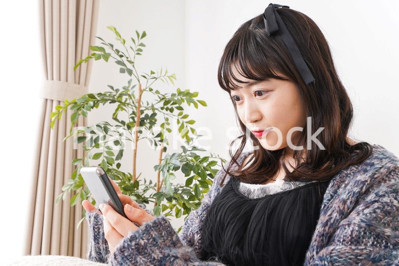 家でスマートフォンを使う若い女性