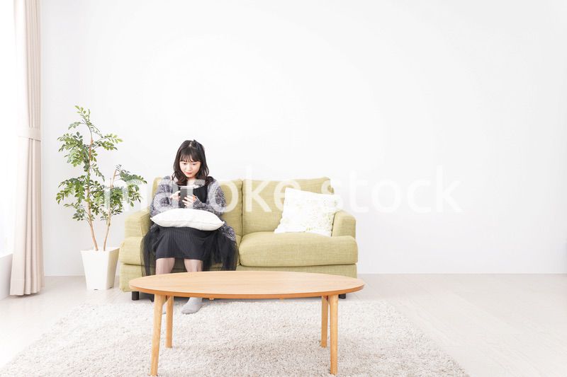 家でスマートフォンを使う若い女性