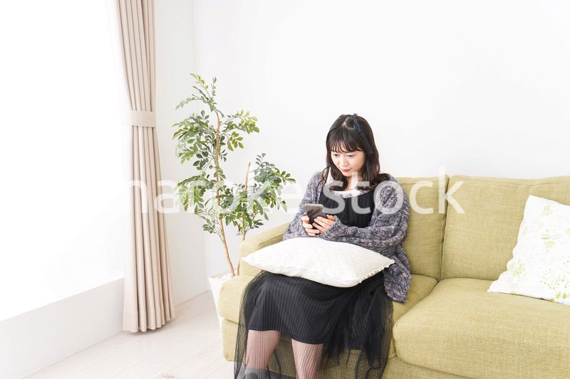 家でスマートフォンを使う若い女性
