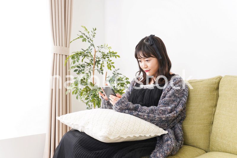 家でスマートフォンを使う若い女性