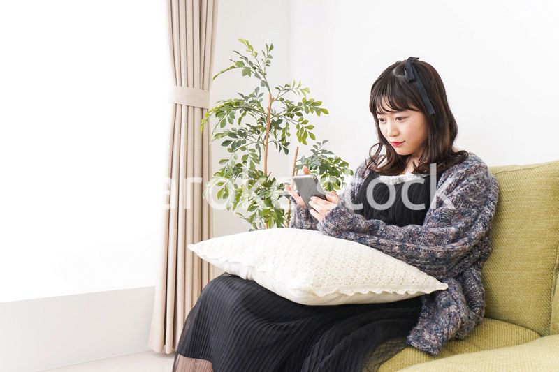 家でスマートフォンを使う若い女性