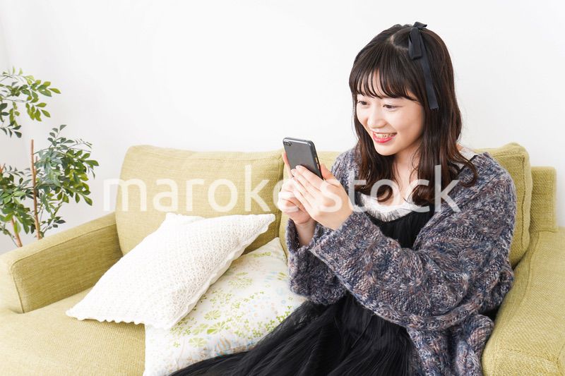 家でスマートフォンを使う若い女性