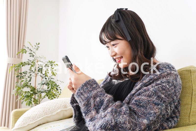 家でスマートフォンを使う若い女性