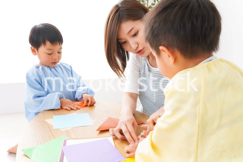 幼稚園で折り紙をする子どもと先生