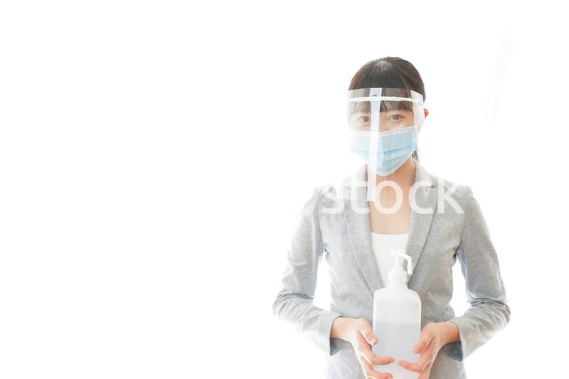 アルコール消毒液を持つフェイスシールドをしたビジネスウーマン