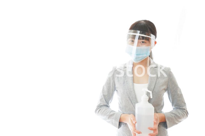 アルコール消毒液を持つフェイスシールドをしたビジネスウーマン