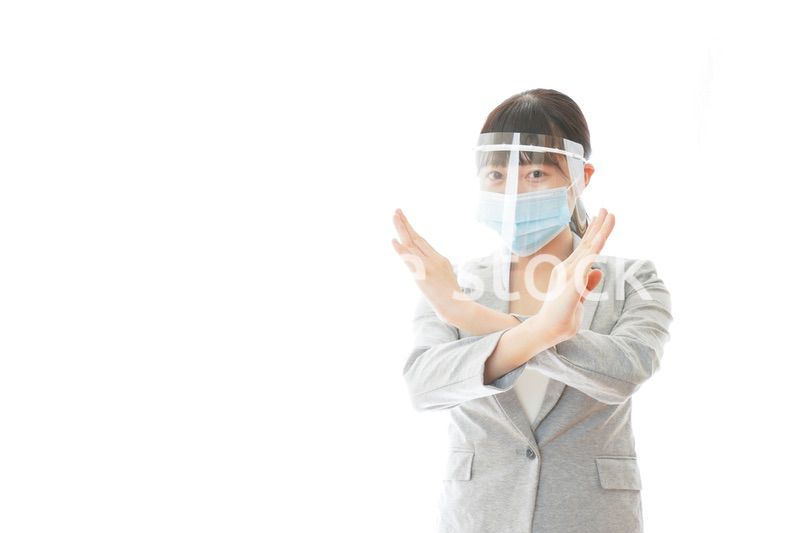 バツサインをするフェイスシールドを装着したビジネスウーマン