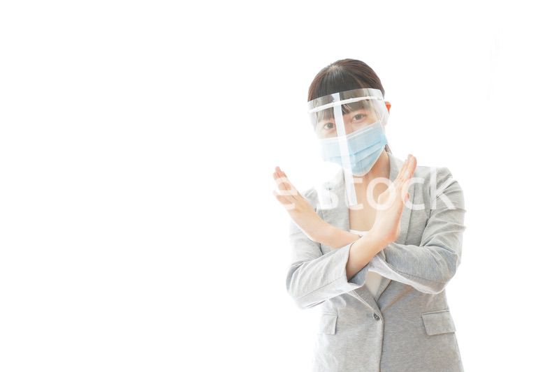 バツサインをするフェイスシールドを装着したビジネスウーマン