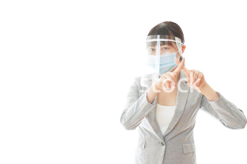 バツサインをするフェイスシールドを装着したビジネスウーマン