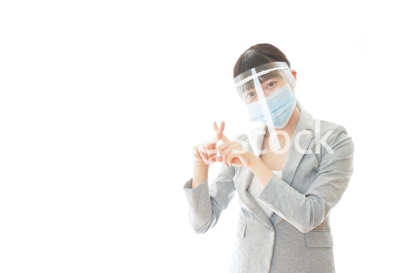 バツサインをするフェイスシールドを装着したビジネスウーマン