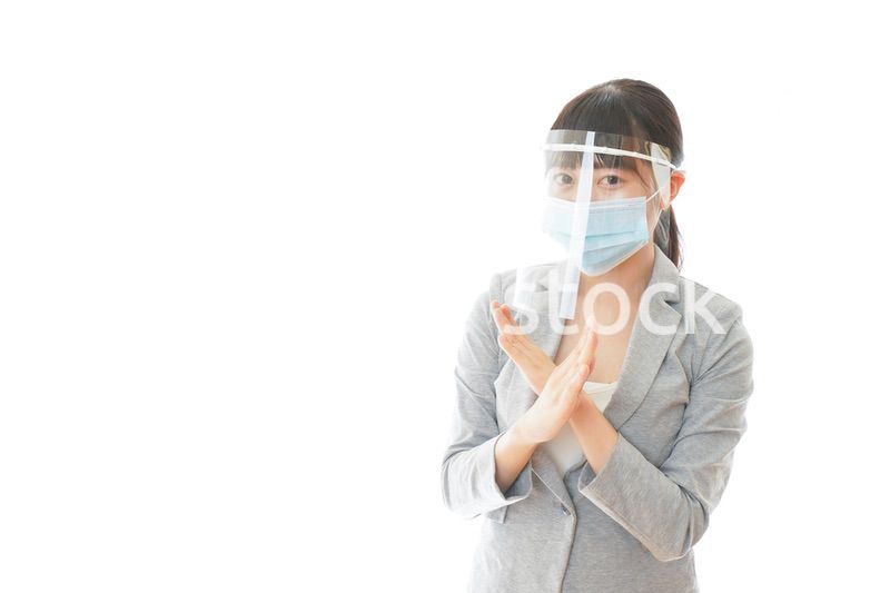 バツサインをするフェイスシールドを装着したビジネスウーマン