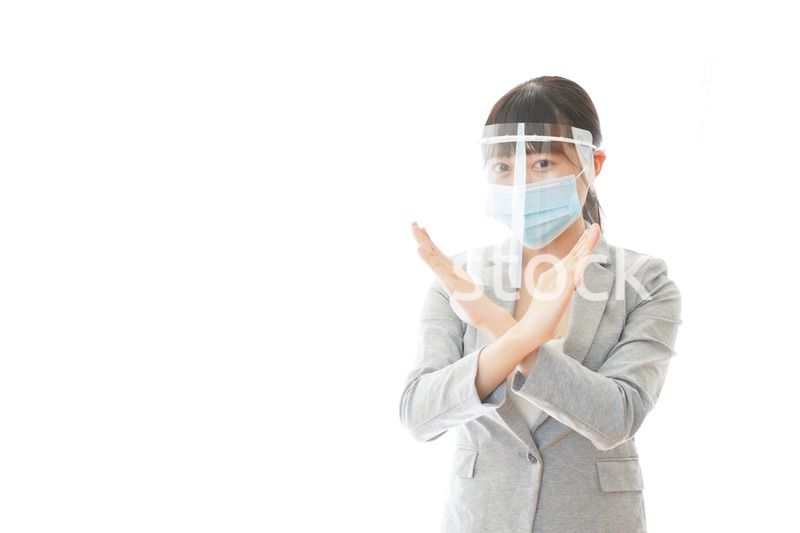 バツサインをするフェイスシールドを装着したビジネスウーマン