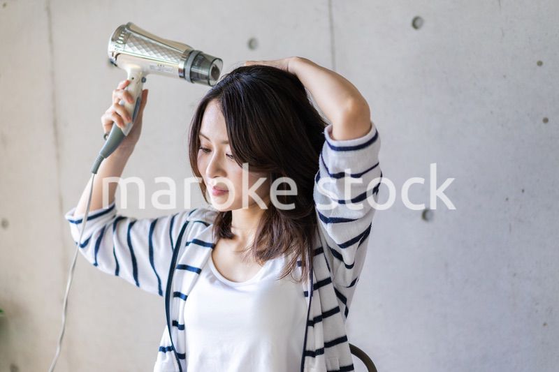 ドライヤーで髪を乾かす若い女性