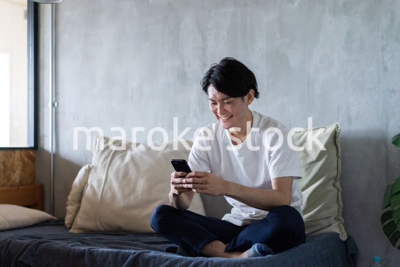 一人暮らしの家でスマホを使う若い男性