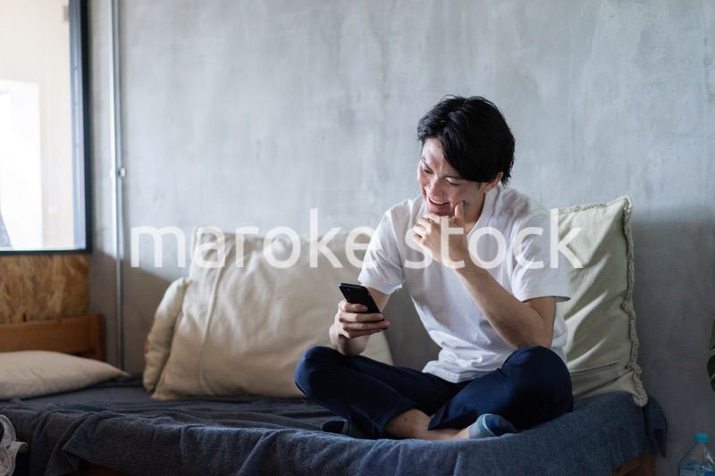 一人暮らしの家でスマホを使う若い男性