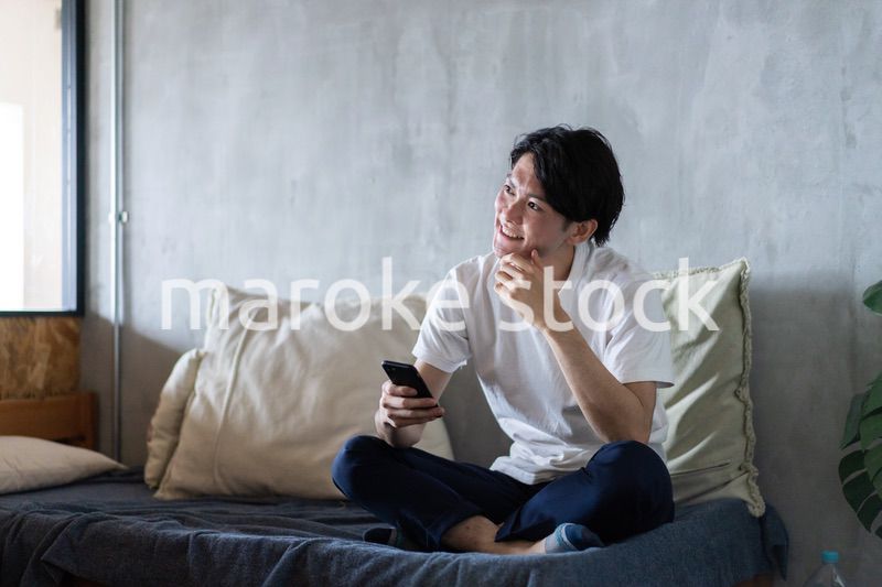 一人暮らしの家でスマホを使う若い男性