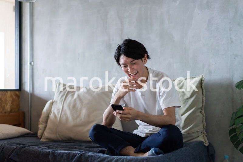 一人暮らしの家でスマホを使う若い男性