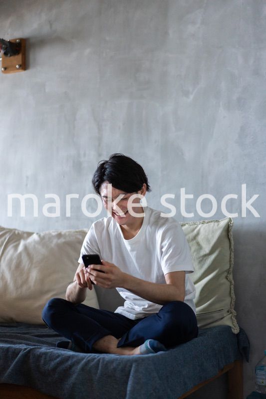一人暮らしの家でスマホを使う若い男性