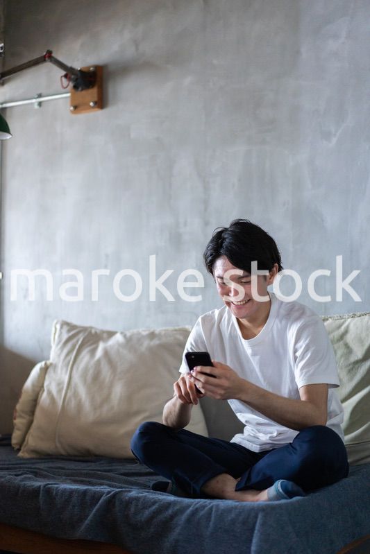 一人暮らしの家でスマホを使う若い男性
