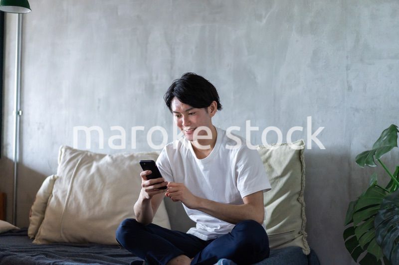 一人暮らしの家でスマホを使う若い男性