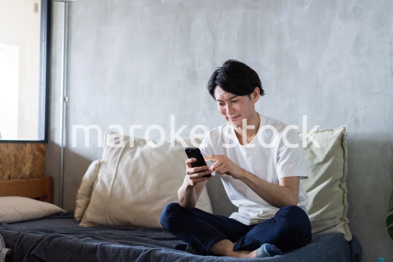 一人暮らしの家でスマホを使う若い男性