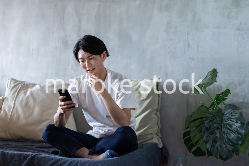 一人暮らしの家でスマホを使う若い男性