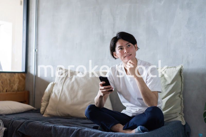 一人暮らしの家でスマホを使う若い男性