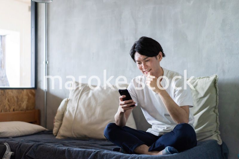 一人暮らしの家でスマホを使う若い男性