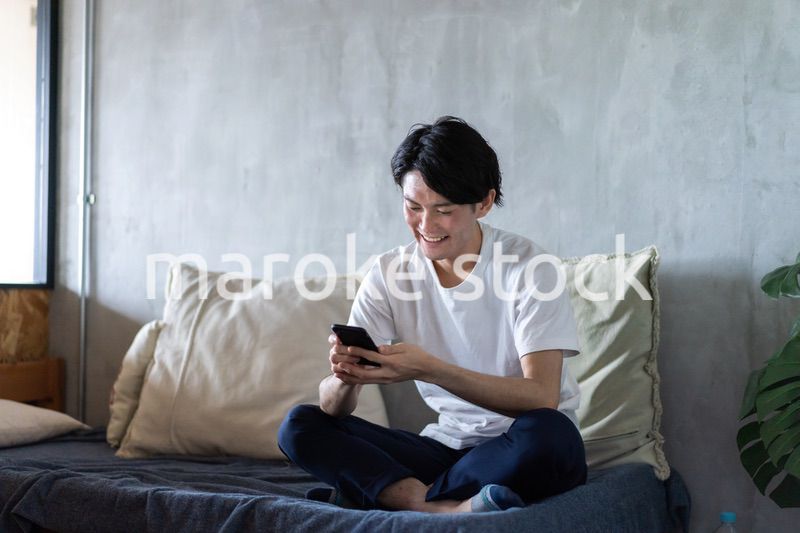 一人暮らしの家でスマホを使う若い男性