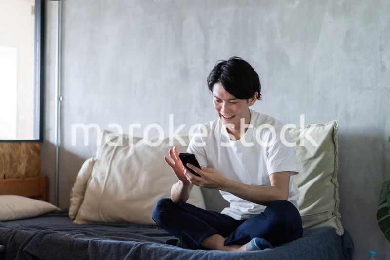 一人暮らしの家でスマホを使う若い男性