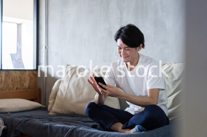 一人暮らしの家でスマホを使う若い男性