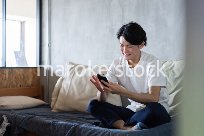 一人暮らしの家でスマホを使う若い男性