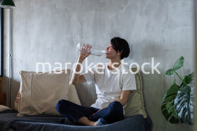 ベッドで水を飲む若い男性
