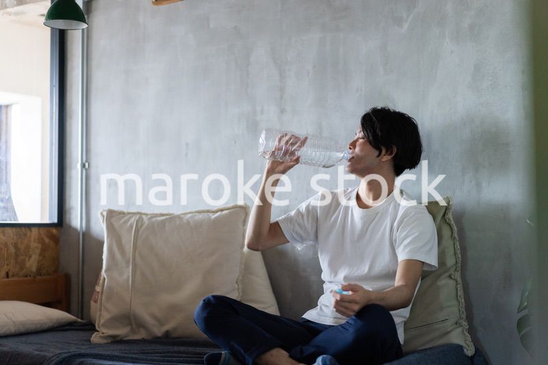 ベッドで水を飲む若い男性