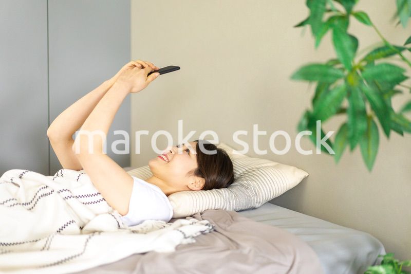ベッドでスマホを使う若い女性