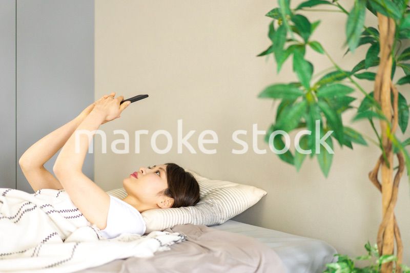 ベッドでスマホを使う若い女性