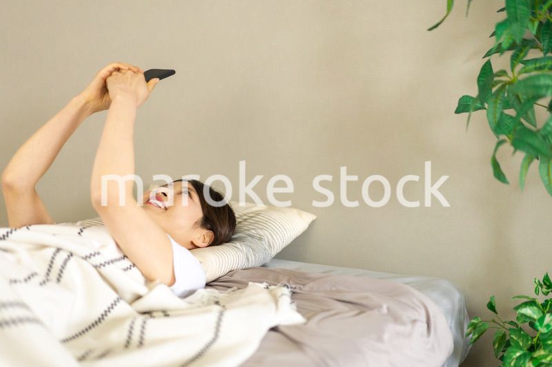 ベッドでスマホを使う若い女性